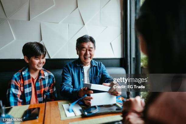 father open a gift box at restaurant - happy birthday grandson images imagens e fotografias de stock