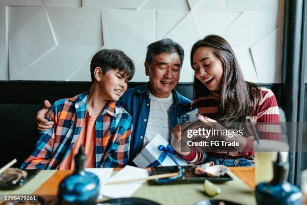 family looking something on mobile phone at restaurant - fathers day dinner stock pictures, royalty-free photos & images