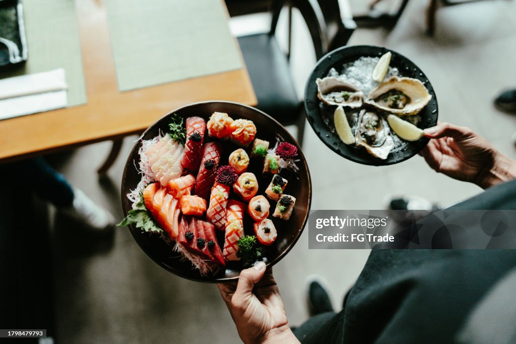 Close-up of a waiter serving japanese food to customer at sushi bar