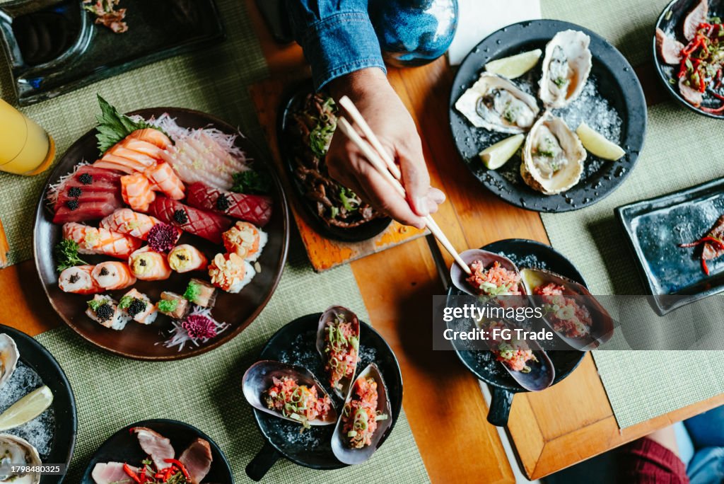 Nahaufnahme einer Person, die Essstäbchen benutzt, um japanisches Essen in einer Sushi-Bar auszuwählen