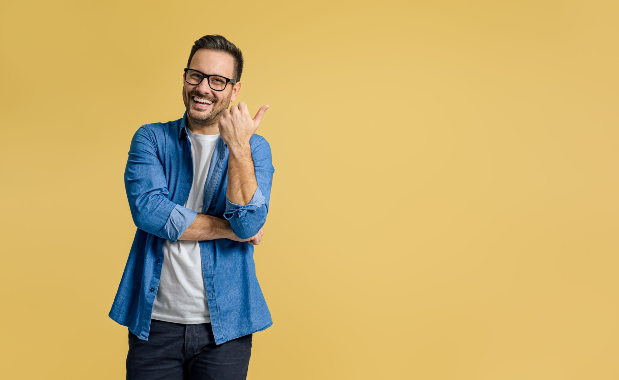 Happy handsome entrepreneur aiming thumb at copy space for advertising against yellow background Happy handsome entrepreneur aiming thumb at copy space for advertising against yellow background