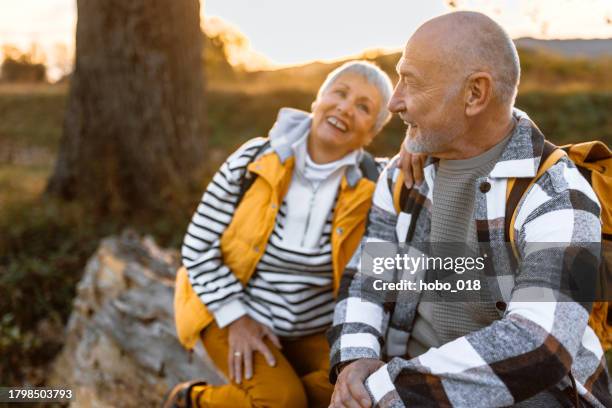 cheerful senior couple having conversation while taking a break from hiking tour - senior couple smiling stock pictures, royalty-free photos & images