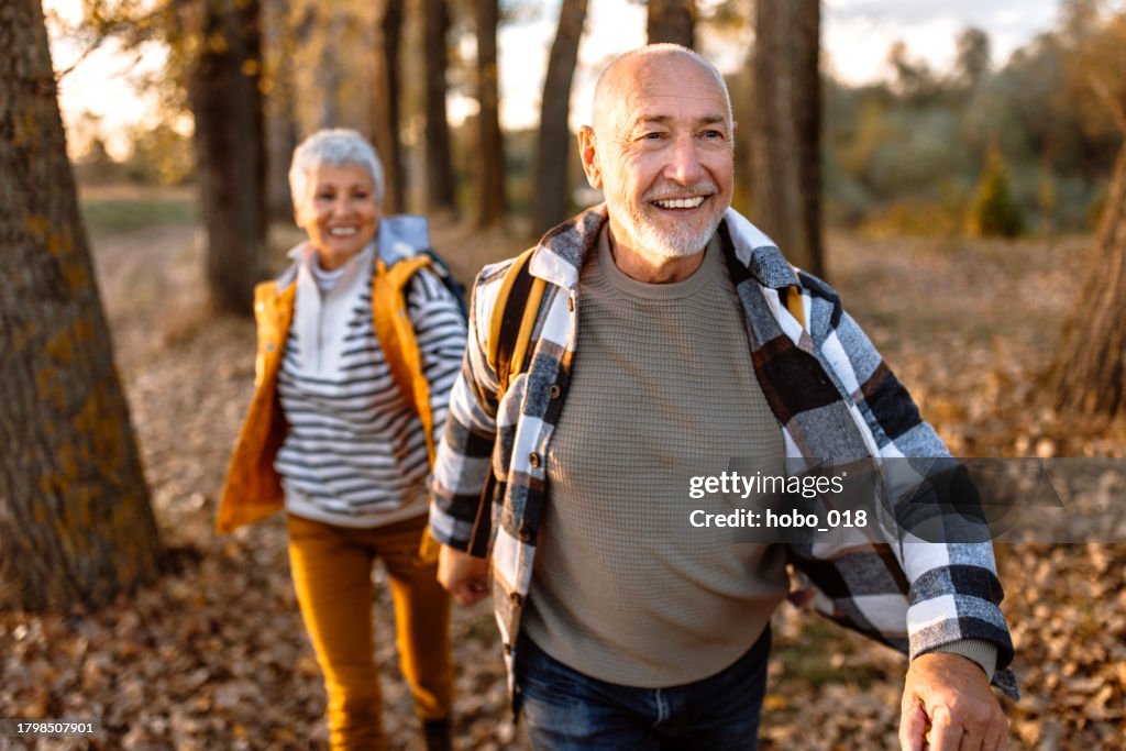 Cheerful senior couple holding hands and running through fallen autumun leaves cover