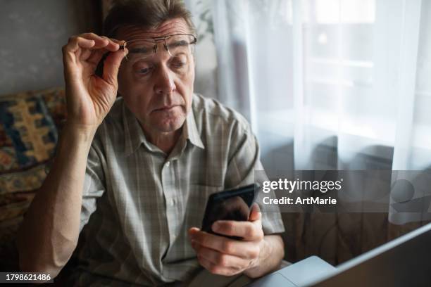 senior man with bad eyesight looking at smartphone at home - astigmatismo imagens e fotografias de stock