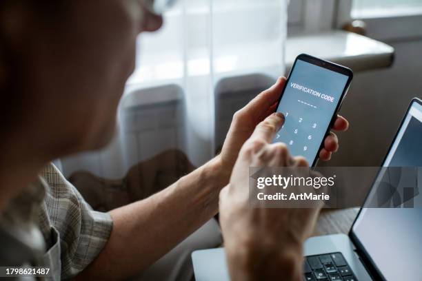 serious senior man at home entering verification code in smartphone, fraud prevention concept. - digitale authenticatie stockfoto's en -beelden