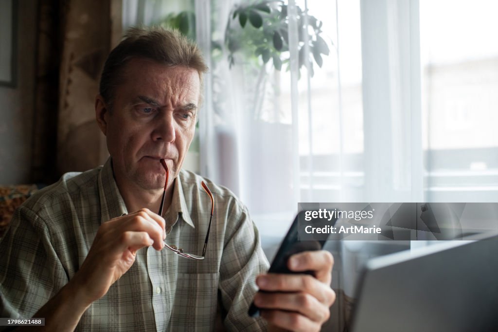 Besorgter älterer Mann, der zu Hause auf sein Smartphone schaut