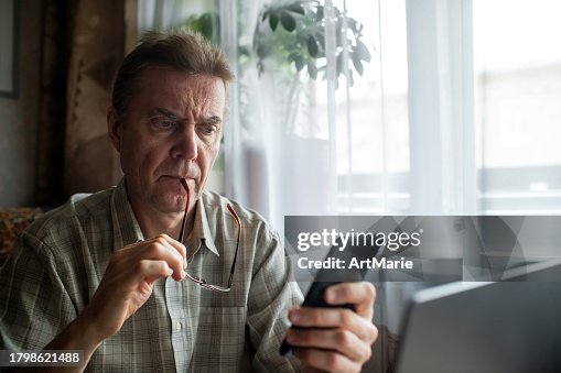 Worried senior man looking at smartphone at home Worried senior man looking at smartphone at home