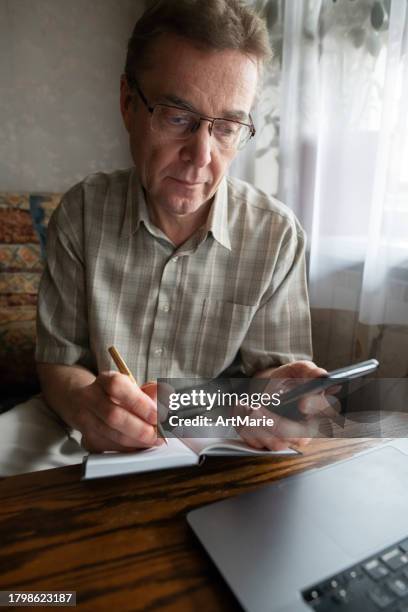 senior man writing down verification code to protect himself from fraud. - forgot password stock pictures, royalty-free photos & images