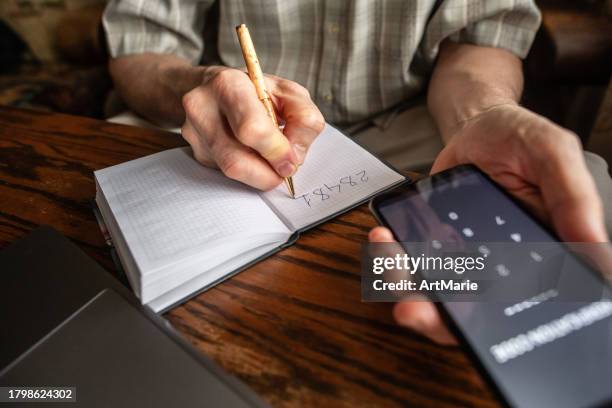 senior man writing down verification code to protect himself from fraud. - report crime stock pictures, royalty-free photos & images