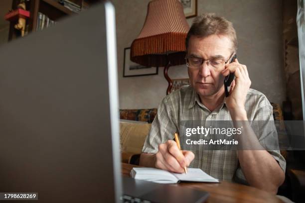 senior man talking by smartphone and writing down important information - fraud prevention stock pictures, royalty-free photos & images