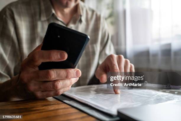 senior man with smartphone  examining  bills, documents or receipts at home - expense fraud stock pictures, royalty-free photos & images