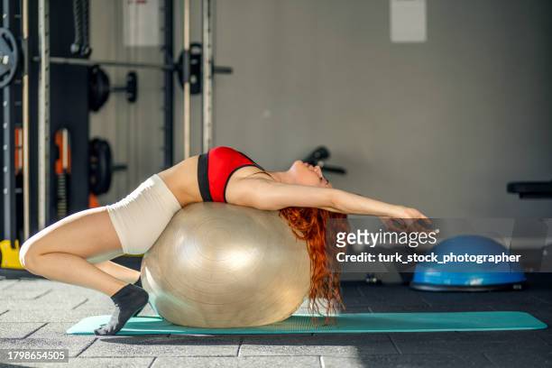 muscular woman stretching with pilates ball in gym - fitness ball imagens e fotografias de stock