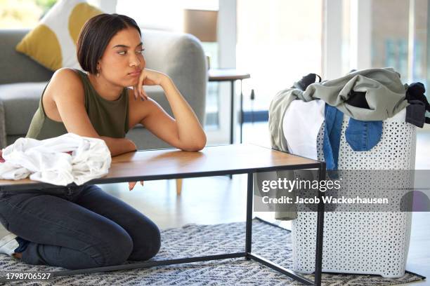 Bored, sad and woman cleaning laundry, housework stress and tired of chaos in the living room. Frustrated, anxiety and cleaner organizing washing clothes, housekeeping and problem with chores