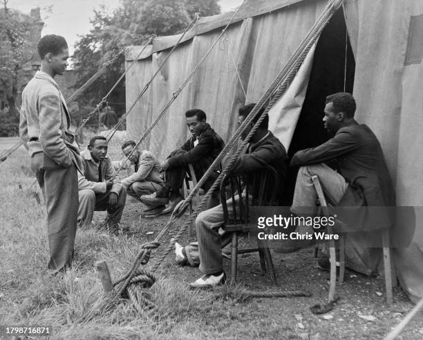 Group of Jamaican men sitting outside a tent as they await interviews with the Ministry of Labour and the Colonial Office ahead of seeking work, in...