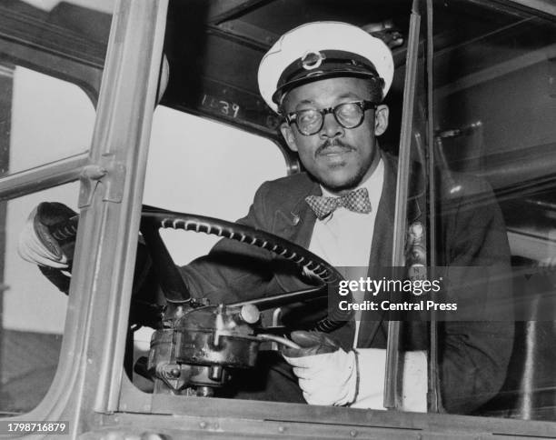 Bespectacled bus driver wearing a checked bow tie in his cab, at the wheel of his bus in London, England, circa 1965.