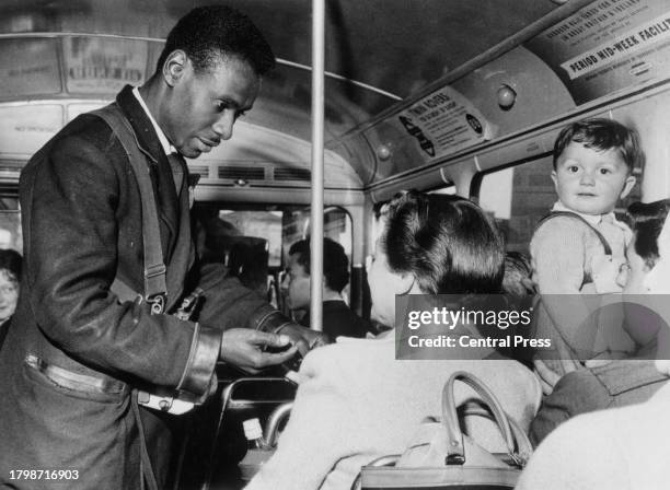 Bus conductor holds out his hand as he collects the fare from a passenger of a bus in London, England, circa 1965.
