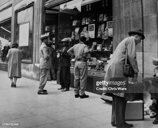 Group of Jamaican men outside a tobacconist shop, two men stand in conversation as two men inspect the window displays, in London, England, United...