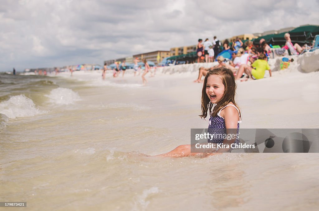 Young girl sitting in the waves, laughing