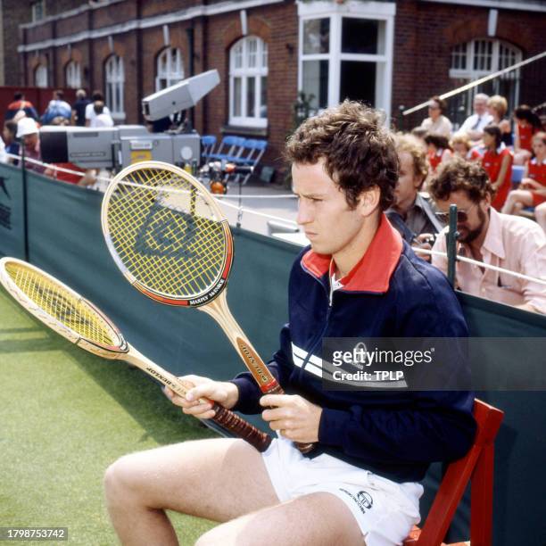American tennis player John McEnroe holds two racquets as he sits at the side of the court at the Queen's Club during the Stella Artois...