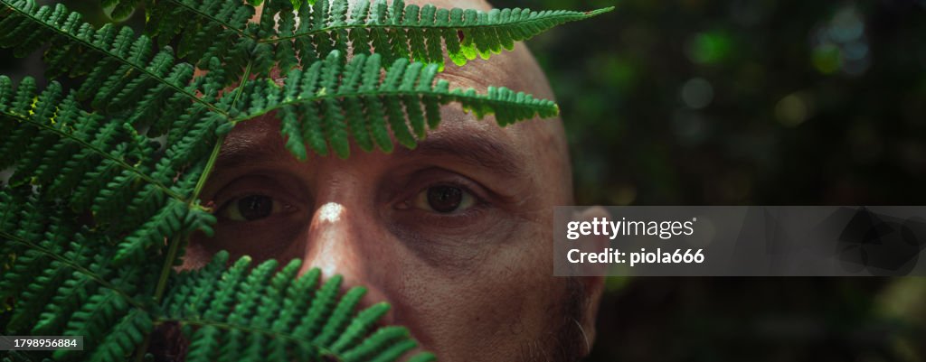Man hiding behind fern in a forest