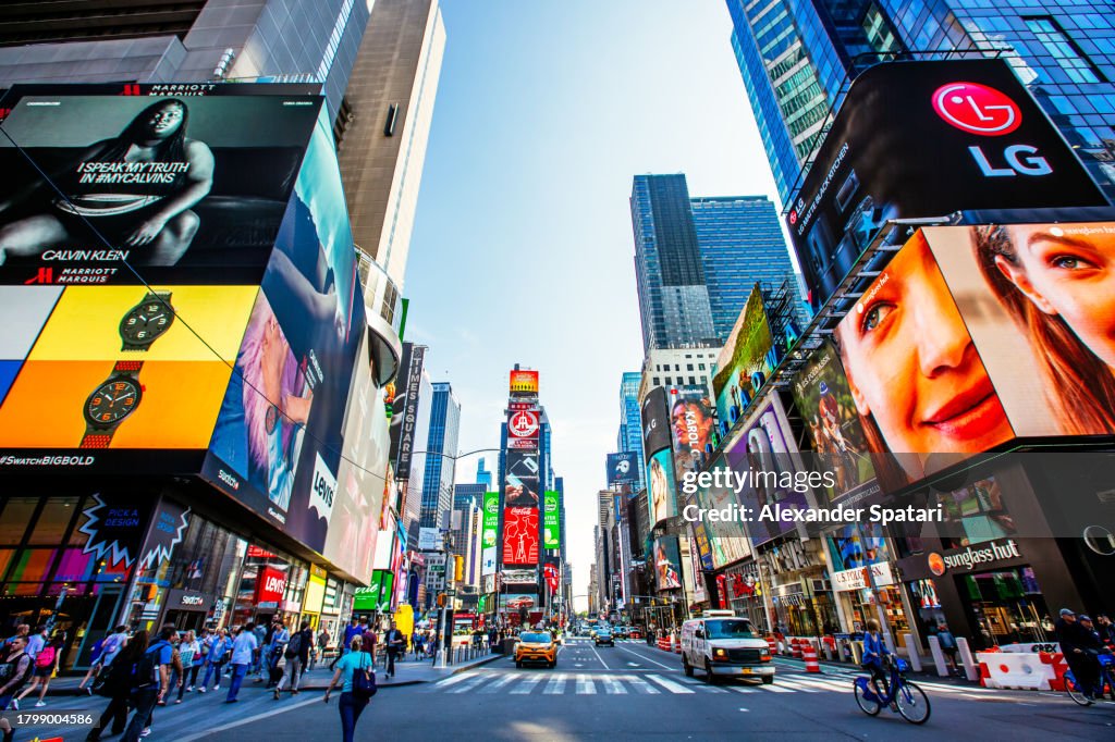 Crowded Times Square with multiple ads on a sunny day with clear blue sky, wide angle view, New York, USA