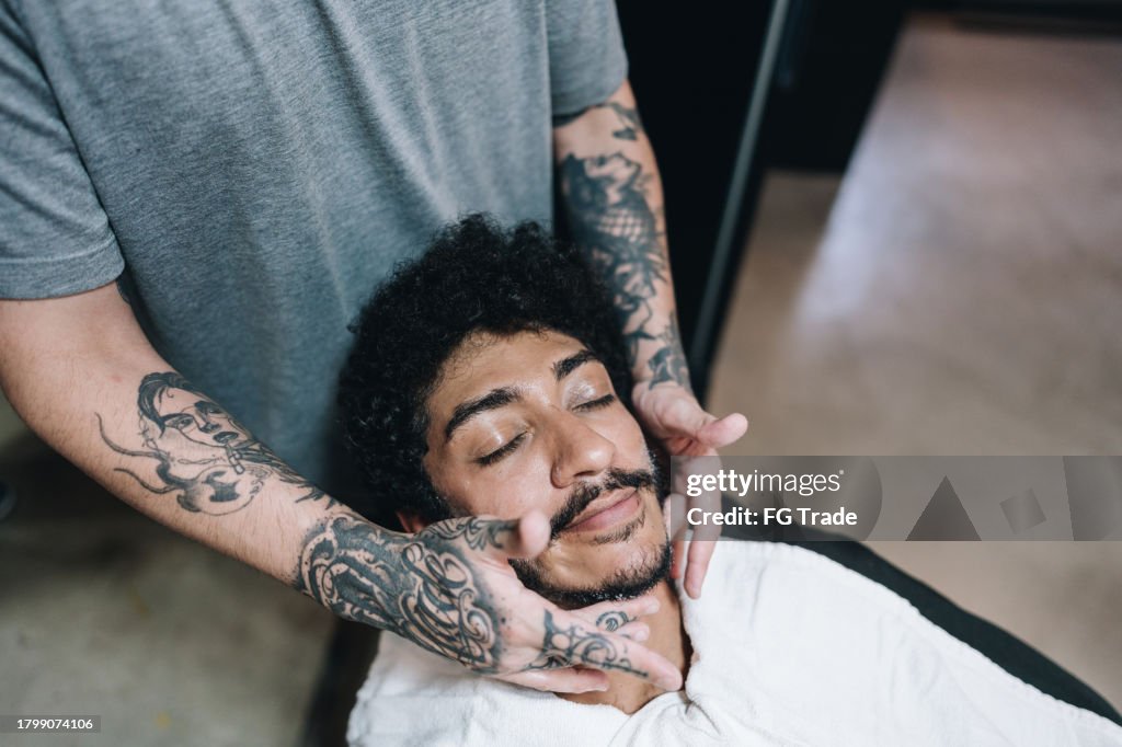 Barber applying beard cream on a customer's beard in a barber shop