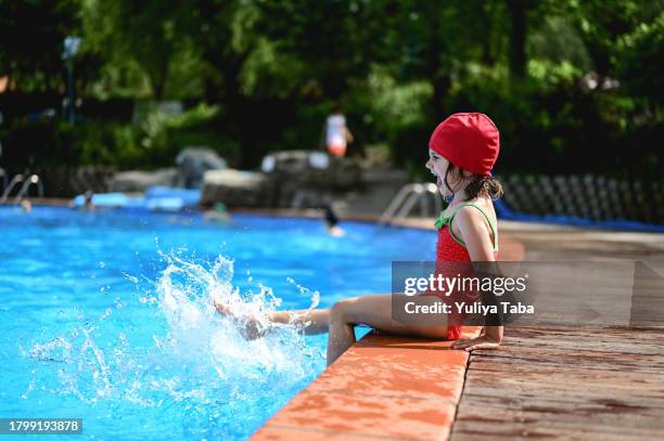 ragazza giocosa in un abbigliamento da bagno rosso che gioca con l'acqua in una piscina. - red hot summer party foto e immagini stock