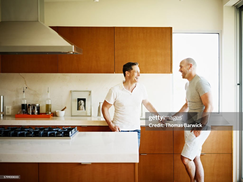 Laughing gay couple standing in kitchen of home