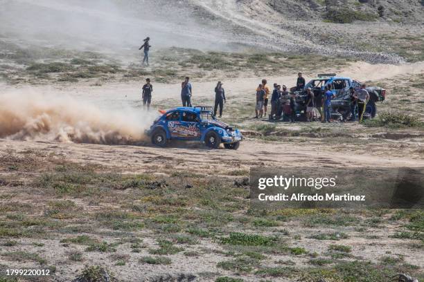 The Geovany Alucano Burgoin racing team in the Class 11 category crosses a sandy section of the dirt road in front of a broken down Trophy Truck...