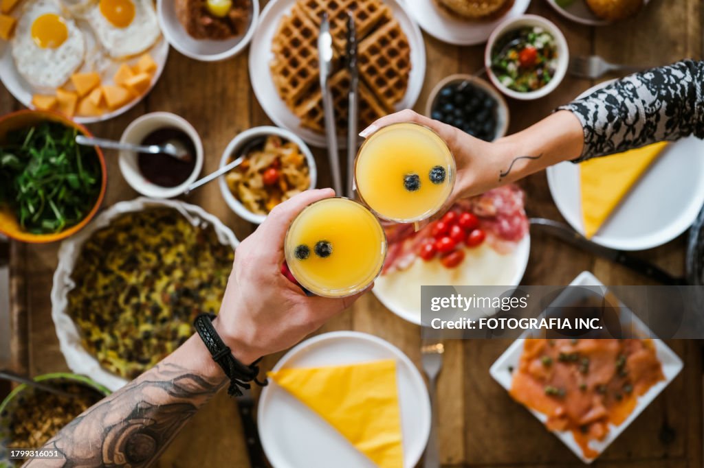 Hands of Young mixed race couple with mimosa cocktails cheering