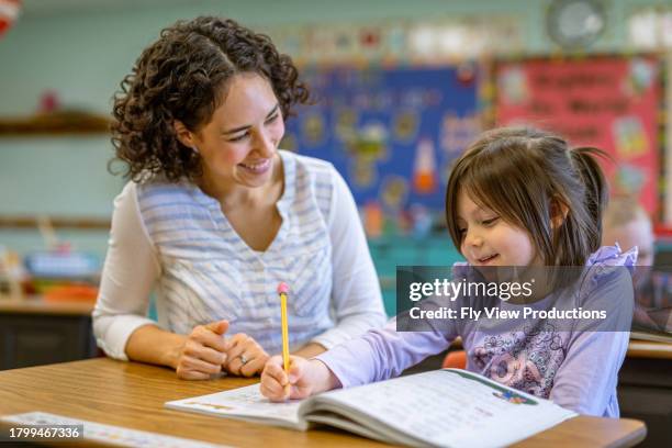 young teacher helps student with classwork - basisschool student stockfoto's en -beelden