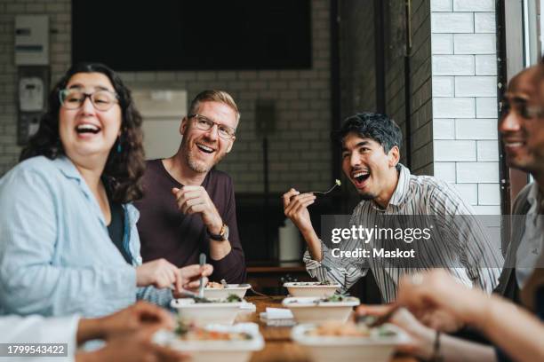 multiracial male and female colleagues having fun while eating lunch together in restaurant - pausa pranzo foto e immagini stock