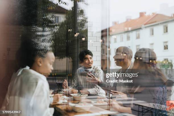 multiracial colleagues discussing while having lunch together seen through window at restaurant - window restaurant stock pictures, royalty-free photos & images