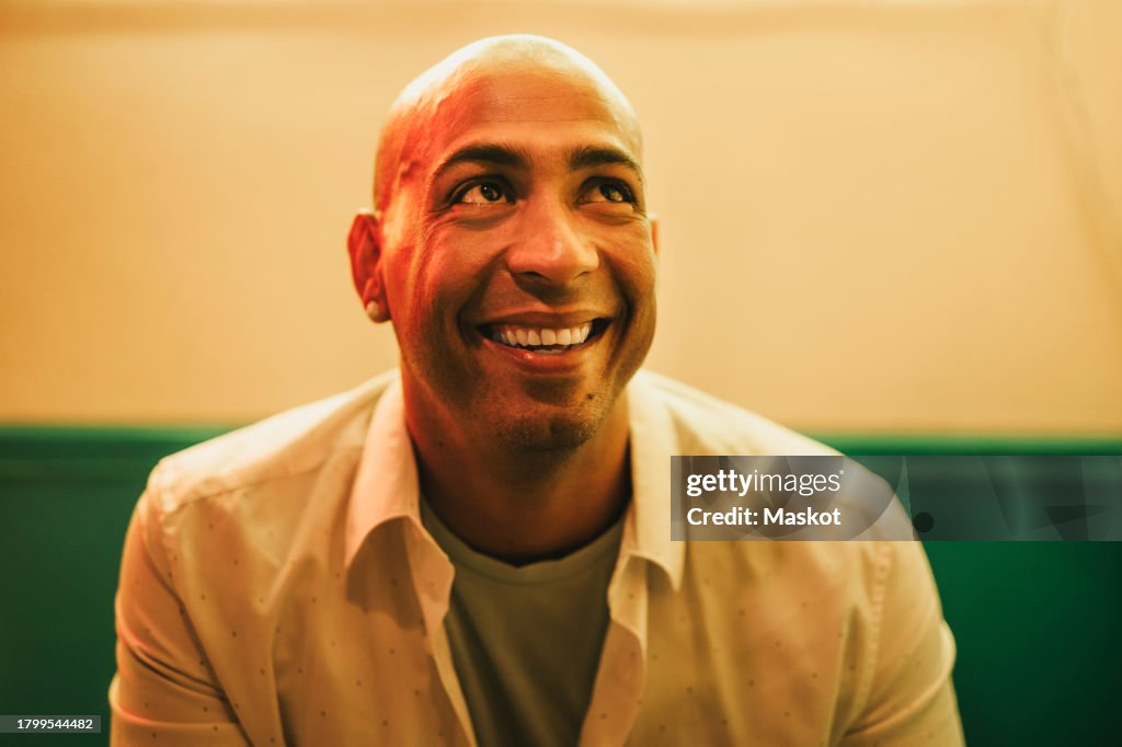 Happy businessman looking up while sitting against wall in cafe