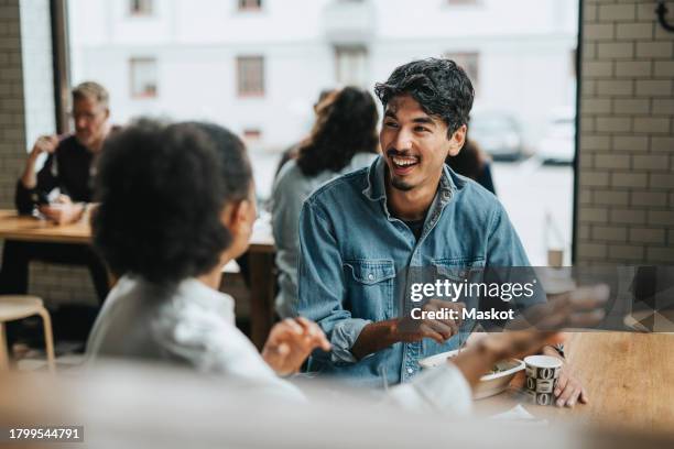 happy multiracial colleagues discussing while having lunch together in restaurant - middle eastern restaurant stock pictures, royalty-free photos & images
