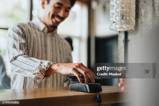 smiling businessman making contactless payment at checkout counter in restaurant - bezahlen stock-fotos und bilder