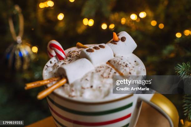 weihnachtliche heiße schokoladentasse mit schneemann aus marshmallows und zuckerstange über weihnachtsbaumhintergrund - kakaopulver stock-fotos und bilder
