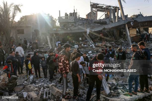 People stand amid the rubble of a building hit during an Israeli strike before the start of a four-day truce in the battles between Israel and Hamas...