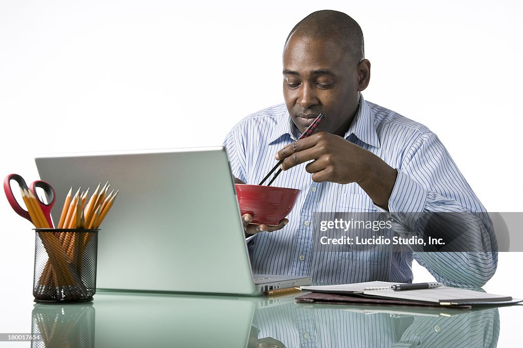 Man eating Asian noodles at work