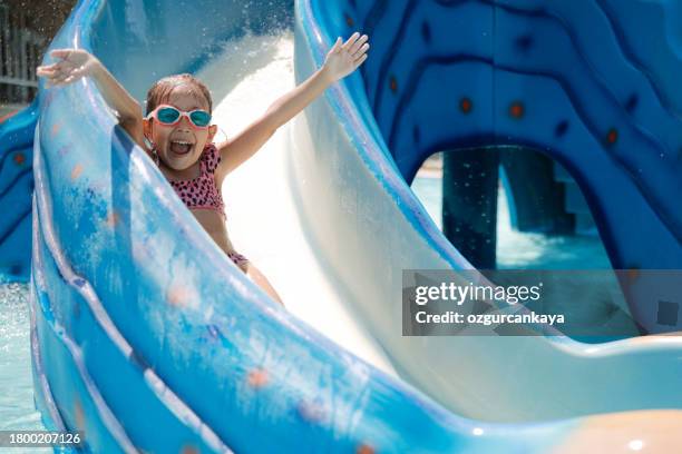 little girl playing on water slide in outdoor pool on a hot summer day - children's slide stockfoto's en -beelden