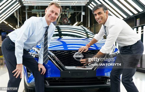 Britain's Prime Minister Rishi Sunak and Britain's Chancellor of the Exchequer Jeremy Hunt pose for a photograph as they attach a Nissan badge to the...