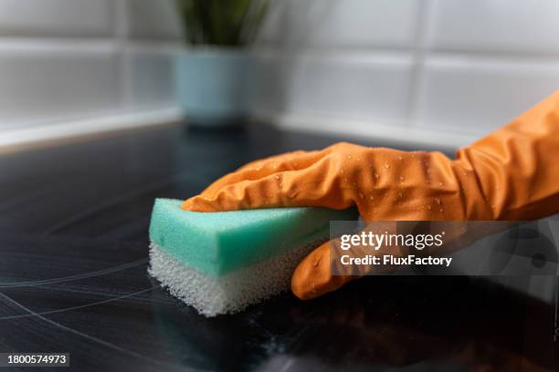 primo piano di una donna che pulisce il piano cottura in vetroceramica con una spugna per la pulizia - spugna per le pulizie foto e immagini stock