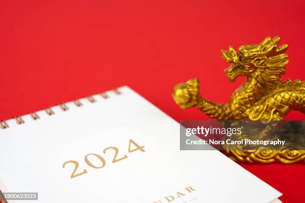 year of the dragon 2024 calendar and golden dragon toy on red background - chinese astrology stock-fotos und bilder