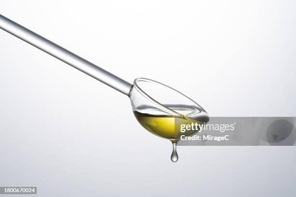 transparent glass spoon filled with olive oil - oil flow stockfoto's en -beelden