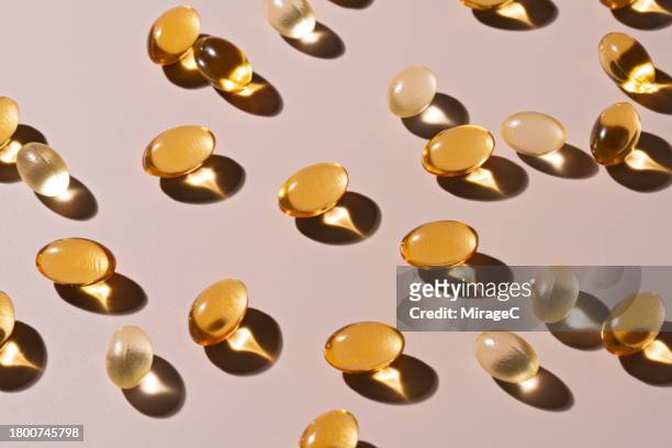 gold colored soft capsules on beige background - huile de foie de morue photos et images de collection