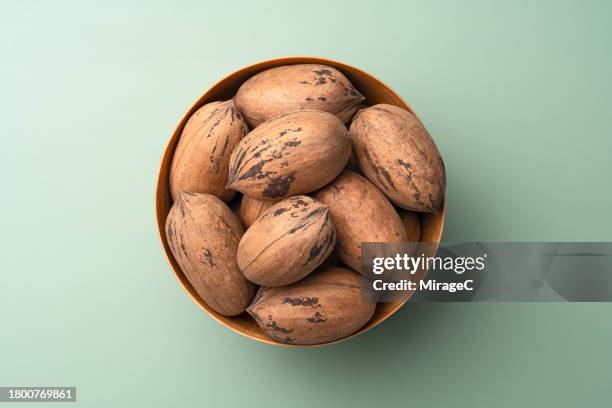 whole pecans in wooden bowl on green background - pecan nut stock pictures, royalty-free photos & images