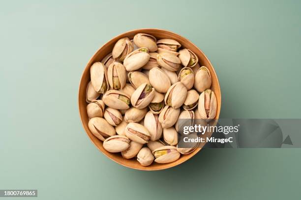 pistachios in wooden bowl on green background - pistachio stock pictures, royalty-free photos & images