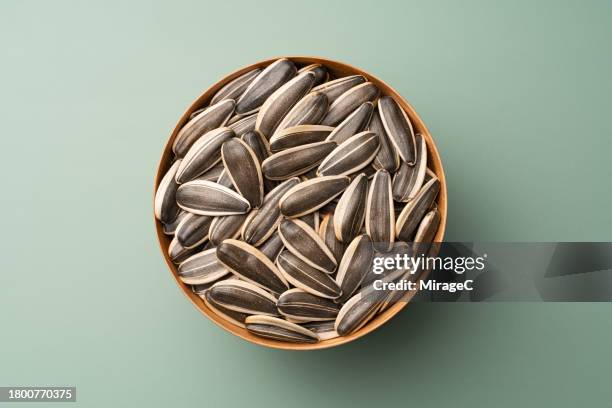 whole sunflower seeds in wooden bowl on green background - sonnenblumenkern stock-fotos und bilder