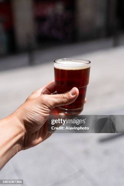 woman hand holding a glass of beer on the street. selective focus. - agarrar stock pictures, royalty-free photos & images