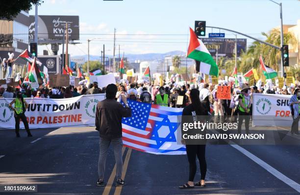 People hold an Israeli and US flag in front of a large group of pro-Palestinian protesters march outside The Grove shopping center on Black Friday,...